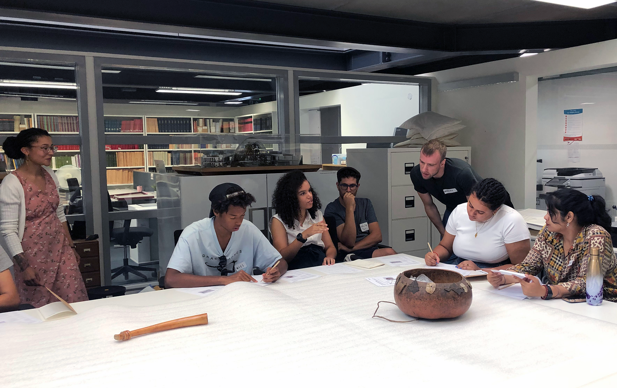 A group of people look closely at objects on a table. 