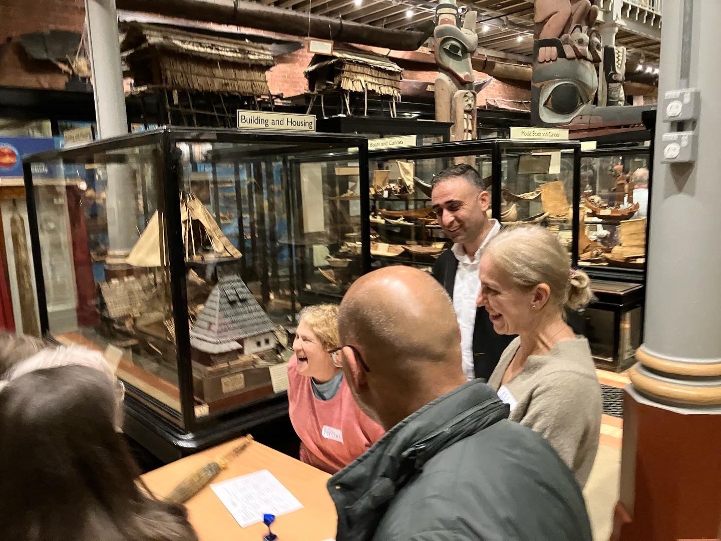 A group of people gather around a table in a museum with crowded glass display cases
