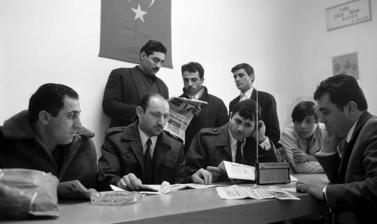 Group of men listening to radio and reading newspapers