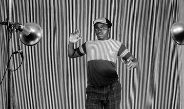 Man posing in front of a striped cloth backdrop. Photograph by Jacques Touselle. Mbouda, Cameroon. About 1980.