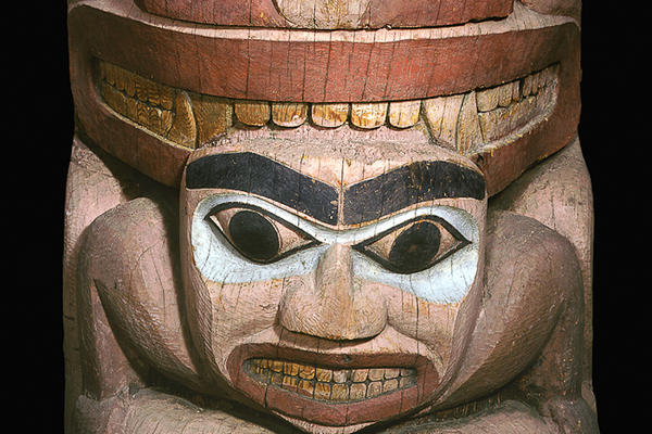 Section of totem pole showing a stylised bear’s face above a man’s face.