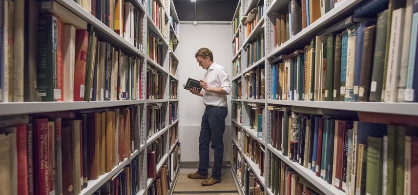Man reading a book between library bookshelves