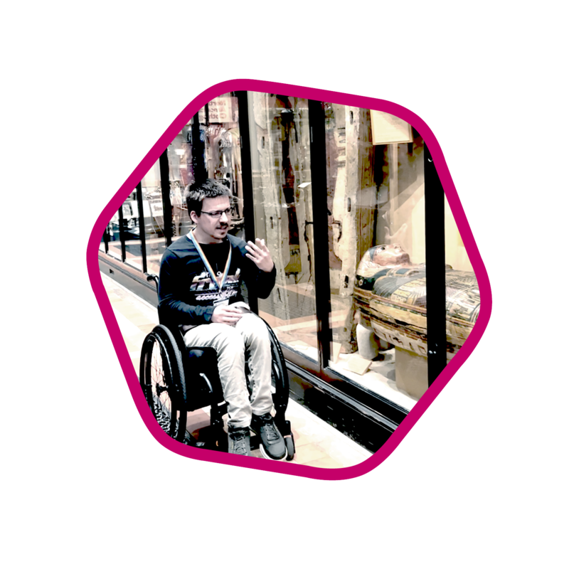 Kyle Lewis Jordan, Curating for Change Fellow at the Pitt Rivers Museum A person in a wheelchair gestures with their hand while talking in front of an Ancient Egypt museum display.