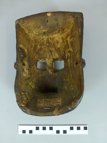 The concave view of a carved wooden mask with two holes for eyes and slot for the mouth. 