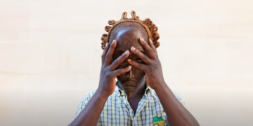 a person holds a wooden mask up their face using both hands