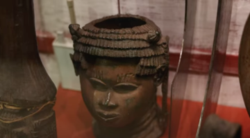 Close up of a Benin bronze on display in the museum, which would have originally held an ivory tusk. A cast metal head with finely sculpted details with a hole in the top.